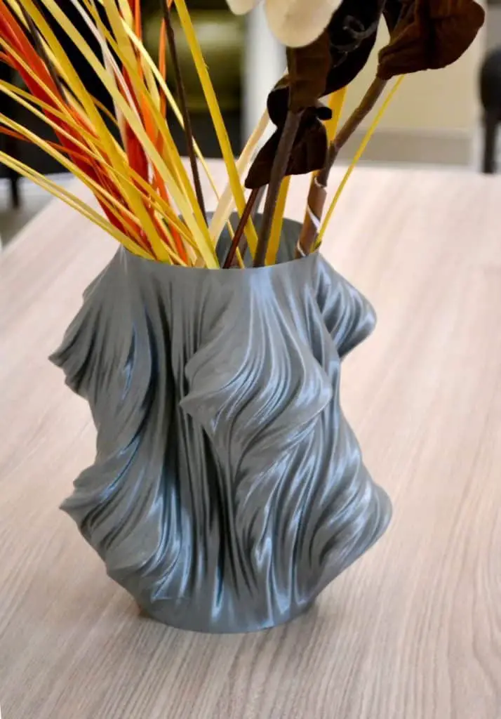 A gray vase printed on a 3d printer stands on a table in the interior
